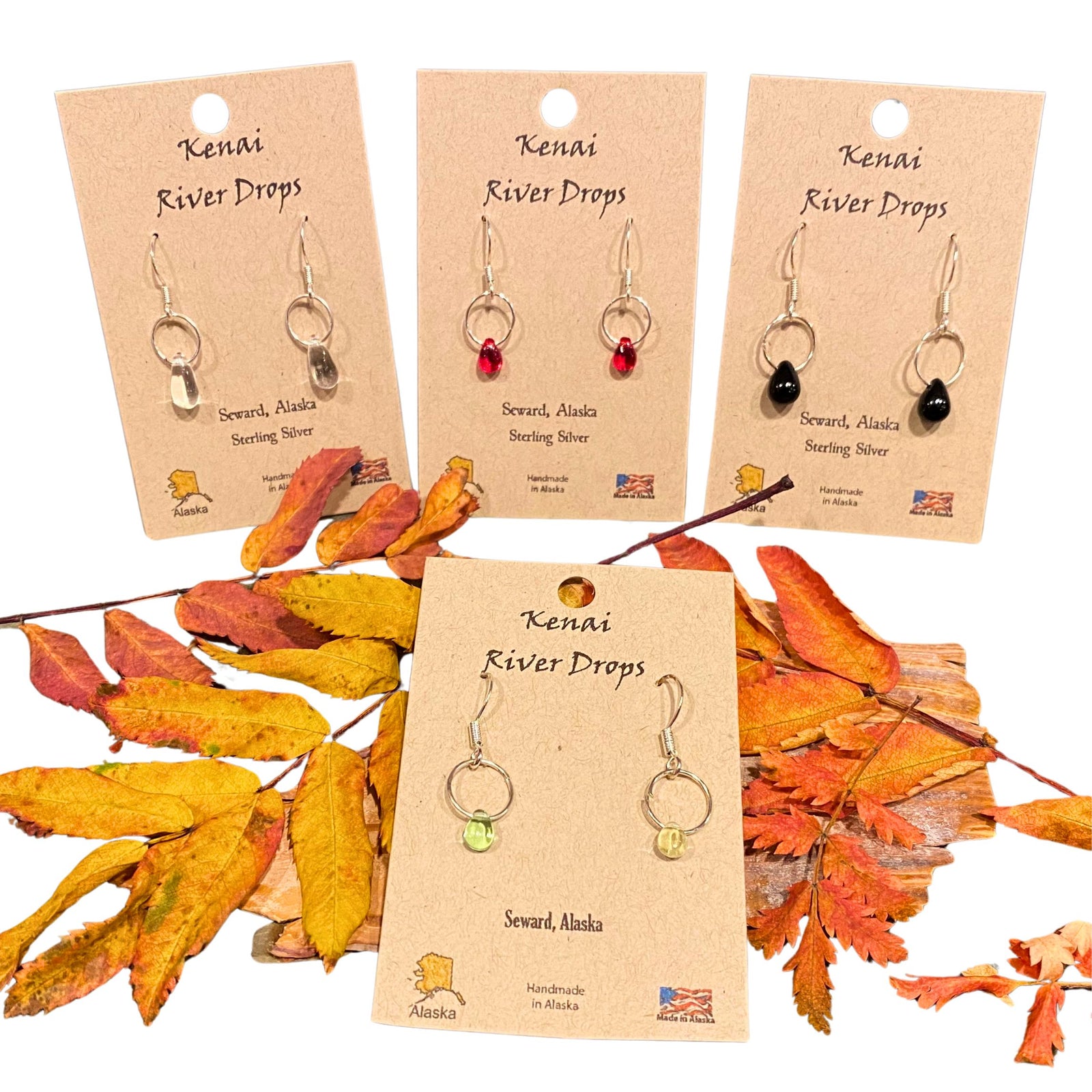 A set of sterling silver earrings displayed on cards with autumn leaves in the background.